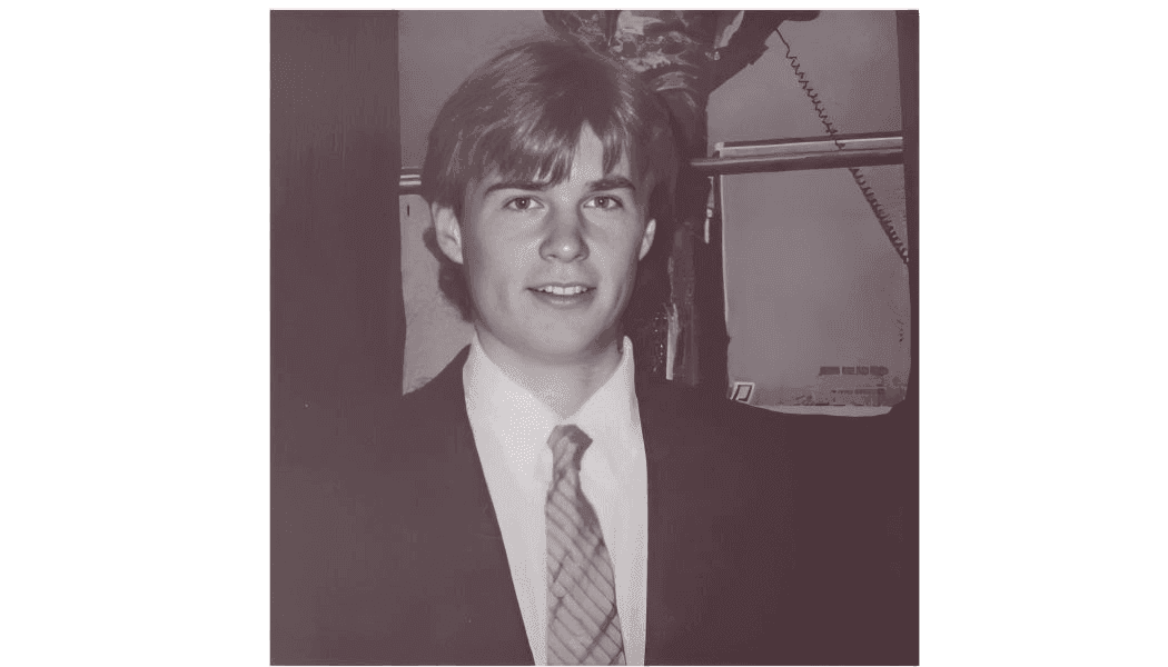 Black and white photo of a young man in a suit and tie, smiling at the camera.